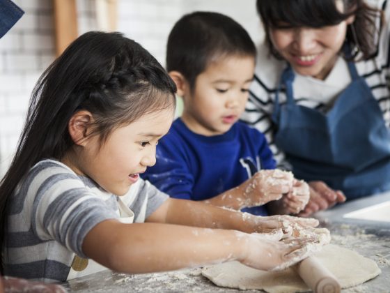 Two young Asian appearance children kneading dough with adult supervision