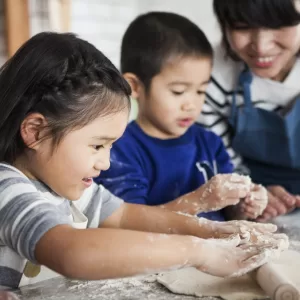 Two young Asian appearance children kneading dough with adult supervision